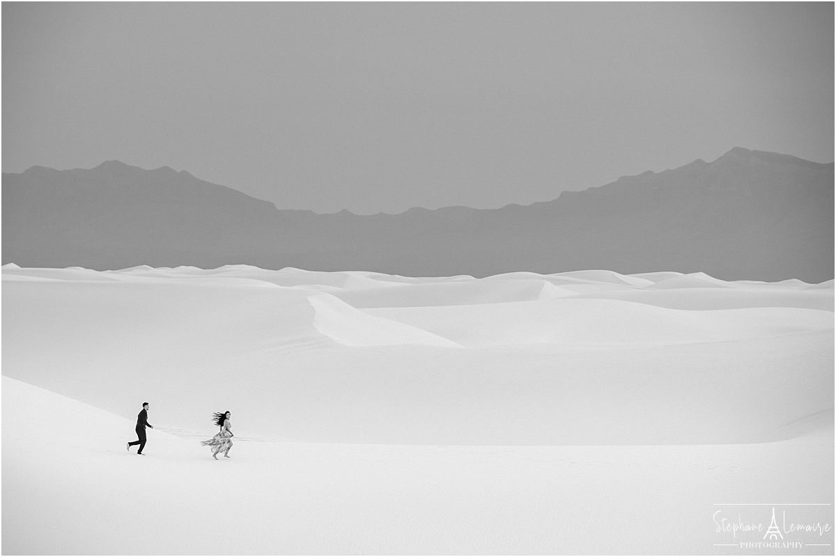 Black and white photograph of couple running at white sands by stephane lemaire photography